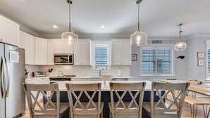 A modern kitchen with white cabinets, a central island with bar stools, a microwave, and pendant lighting. - Sweet Serendipity - Close to beach, Greenway, and popular restaurants and bars. (Carolina Beach)