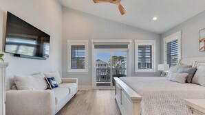 A bedroom with a large bed, a sofa, and a TV mounted on the wall. - Sweet Serendipity - Close to beach, Greenway, and popular restaurants and bars. (Carolina Beach)