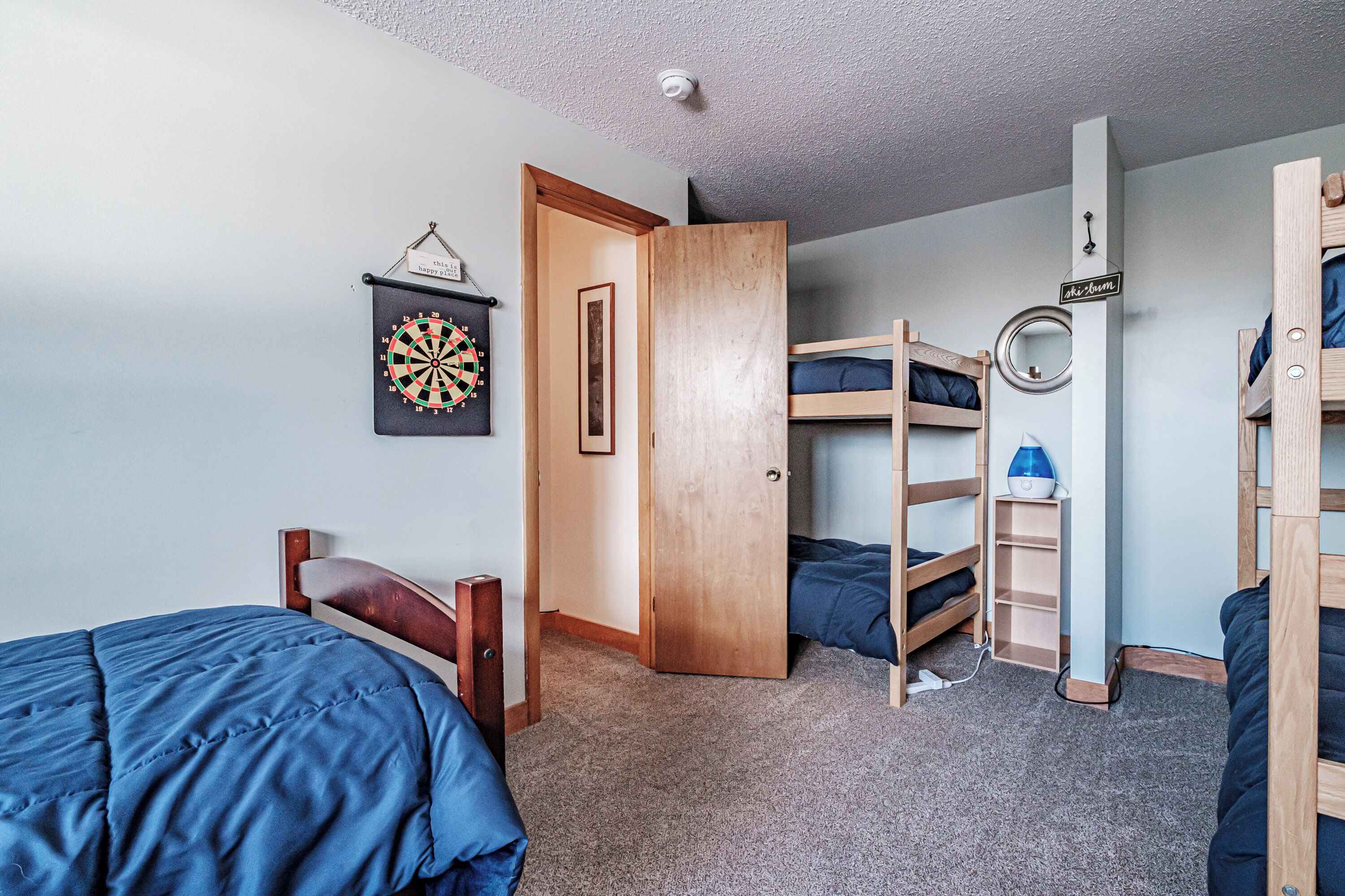 A bedroom with bunk beds, a dartboard, and a door leading to another room.