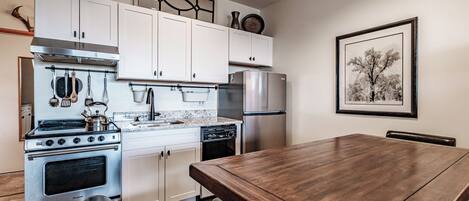 A modern kitchen with white cabinets, stainless steel appliances, and a wooden dining table.