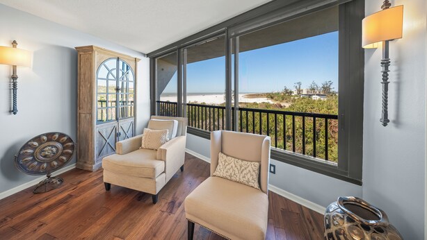 Una habitación con dos sillones color beige, un aparador de madera y un ventanal con vista a la playa.
