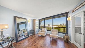 A spacious room with hardwood flooring, a large mirror, a sofa, and a view of the beach through large windows. - Discover Gulf and Bay Club Unit F407 in Siesta Key! (Siesta Key)