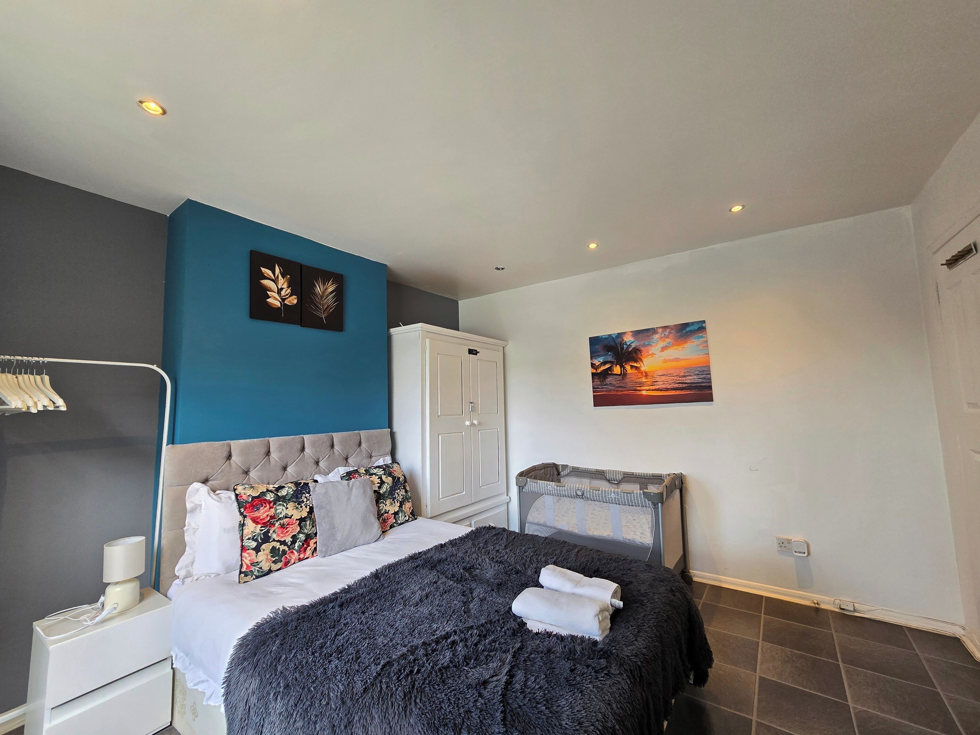A bedroom with a bed, nightstand, wardrobe, and artwork on the walls.