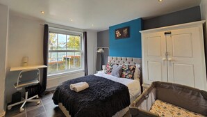 A bedroom with a bed, a desk, a chair, a wardrobe, and a window with a view of the outside.