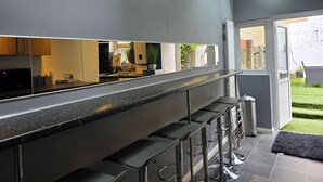 A modern kitchen with a bar area, large windows, and a view of the garden.