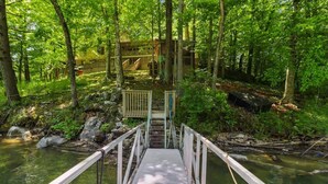 Un puente de madera que conduce a un edificio rodeado de un bosque frondoso y un arroyo cristalino.