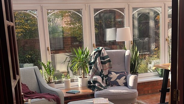 A conservatory with a glass ceiling, a grey sofa, a patterned rug, and potted plants. - St Albans Spacious Party House (St Albans)