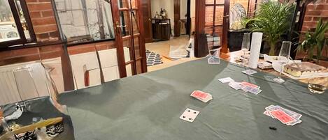 A room with a brick wall, a framed picture, and a table with playing cards and glasses.