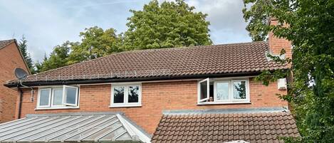A two-story brick house with a conservatory, a patio with a bench, and a garden.