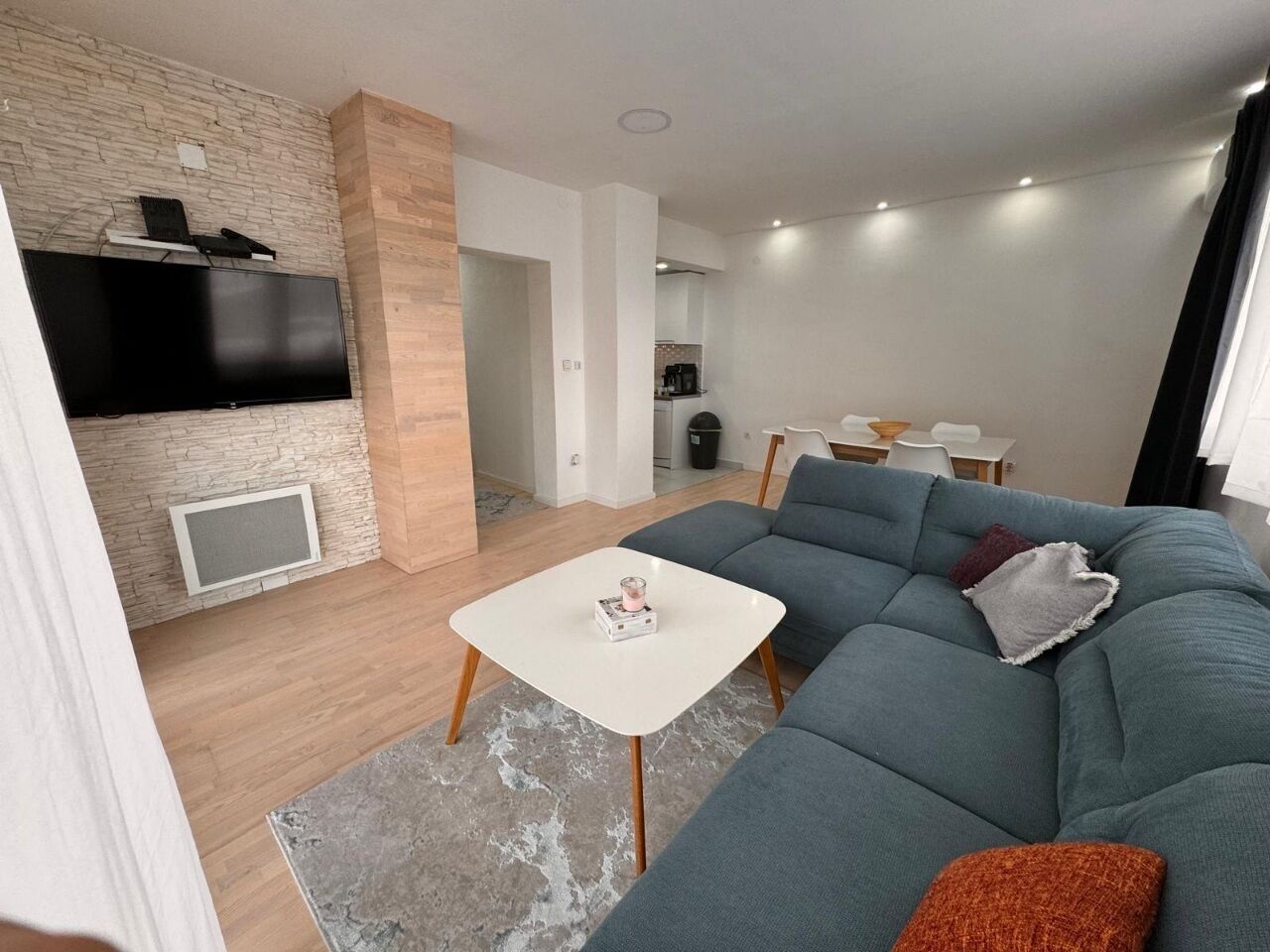 Een moderne woonkamer met een grijze modulaire bank, een witte salontafel en een flatscreen televisie bevestigd aan een stenen muur.