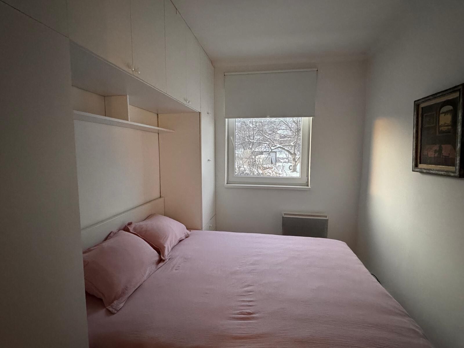 Una camera da letto con un letto, una finestra vista alberi e mobili contenitori integrati.