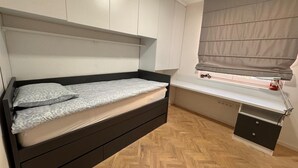Une chambre à coucher comprenant un lit, des rangements intégrés, un bureau et une fenêtre avec des stores.