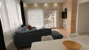 Un salon moderne avec un canapé d’angle gris, une table à manger blanche et un saladier en bois posé sur la table.
