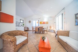 Uma sala de estar ampla com móveis de vime, um espaço de jantar e uma cozinha ao fundo.