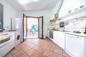 Uma cozinha moderna com armários brancos, forno embutido, lava-louças e uma janela grande que se abre para um pátio.