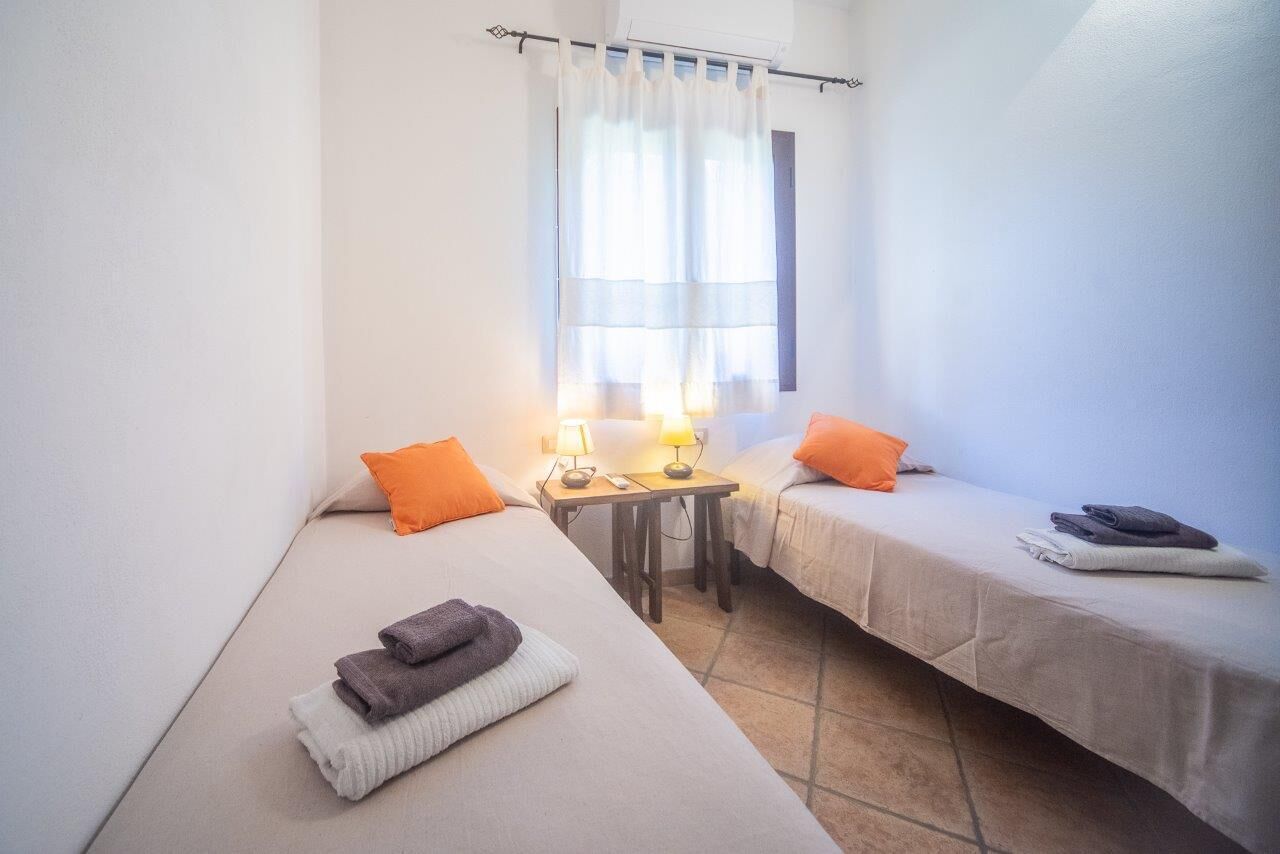 A small, clean room with two single beds, a table with lamps, and a window with curtains.