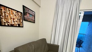 Ein Wohnzimmer mit einem braunen Sofa, einem gerahmten Bild an der Wand und Blick auf einen Balkon mit einem Stuhl.