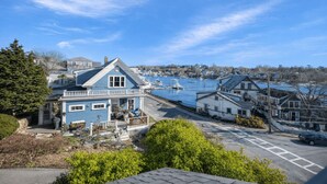 A coastal town with a prominent blue house with a balcony, a marina with boats, and a clear blue sky. - Painter's Perch: Rocky Neck (Gloucester)