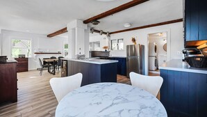 A modern kitchen with a marble island, wooden beams, and a dining area with a round table. - Painter's Perch: Rocky Neck (Gloucester)