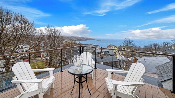 A deck with two white Adirondack chairs and a glass table, overlooking a snowy landscape and a body of water. - Portside Overlook: Downtown Rockport Penthouse with stunning views (Rockport)