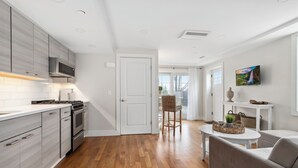 Una cocina moderna con piso de madera, electrodomésticos de acero inoxidable y un comedor con mesa y sillas blancas.