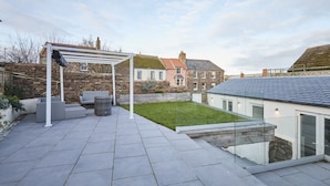 A patio with a pergola, outdoor seating, and a grassy area. - Host & Stay | Harrow Bothy (Tweedmouth)