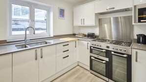 A modern kitchen with white cabinets, a stainless steel range, and a window with a view of a snowy landscape. - Host & Stay | Harrow Bothy (Tweedmouth)