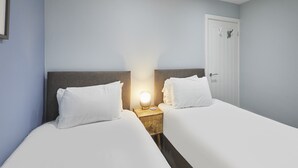 A hotel room with two single beds, a nightstand with a lamp, and a door with a coat hook. - Host & Stay | Harrow Bothy (Tweedmouth)