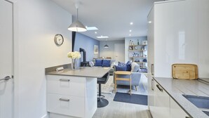 A modern kitchen with white cabinets, a central island, and a dining area with a sofa and table. - Host & Stay | Harrow Bothy (Tweedmouth)