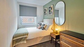 A bedroom with a bed, a bedside table, a dresser, a window with a blind, and wall art. - Host & Stay | Joffre Avenue (Castleford)