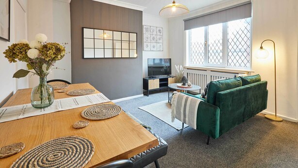 A modern living room with a wooden dining table, green sofa, and a TV. - Host & Stay | Joffre Avenue (Castleford)