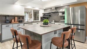 Una cocina moderna con una isla central, electrodomésticos de acero inoxidable y una zona de estar con sillas.