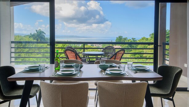 Comedor con una mesa lista para cuatro, con vistas a un paisaje exuberante, el mar y las montañas.