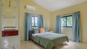 Un dormitorio con cama, mesita de noche, cortinas en la ventana y aire acondicionado.