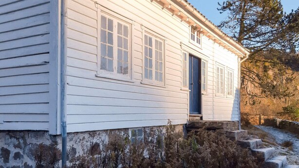 A white wooden house with a blue door, a small porch, and a stone wall foundation. - 5 Person Holiday Home in Lyngdal (Lyngdal)