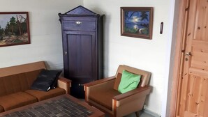 A living room with a brown sofa, a small table, a cabinet, and a chair with a green pillow. - 5 Person Holiday Home in Lyngdal (Lyngdal)