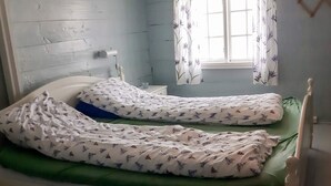 A single-bed room with a green mattress, white bedding with a pattern, a window with floral curtains, and a white-painted wall. - 5 Person Holiday Home in Lyngdal (Lyngdal)