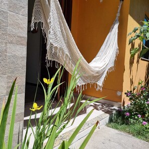 Relax in a serene garden setting, surrounded by lush greenery and vibrant flowers, with a hammock suspended between two buildings.