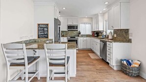 A modern kitchen with white cabinetry, a granite countertop, and a dining area with white chairs.