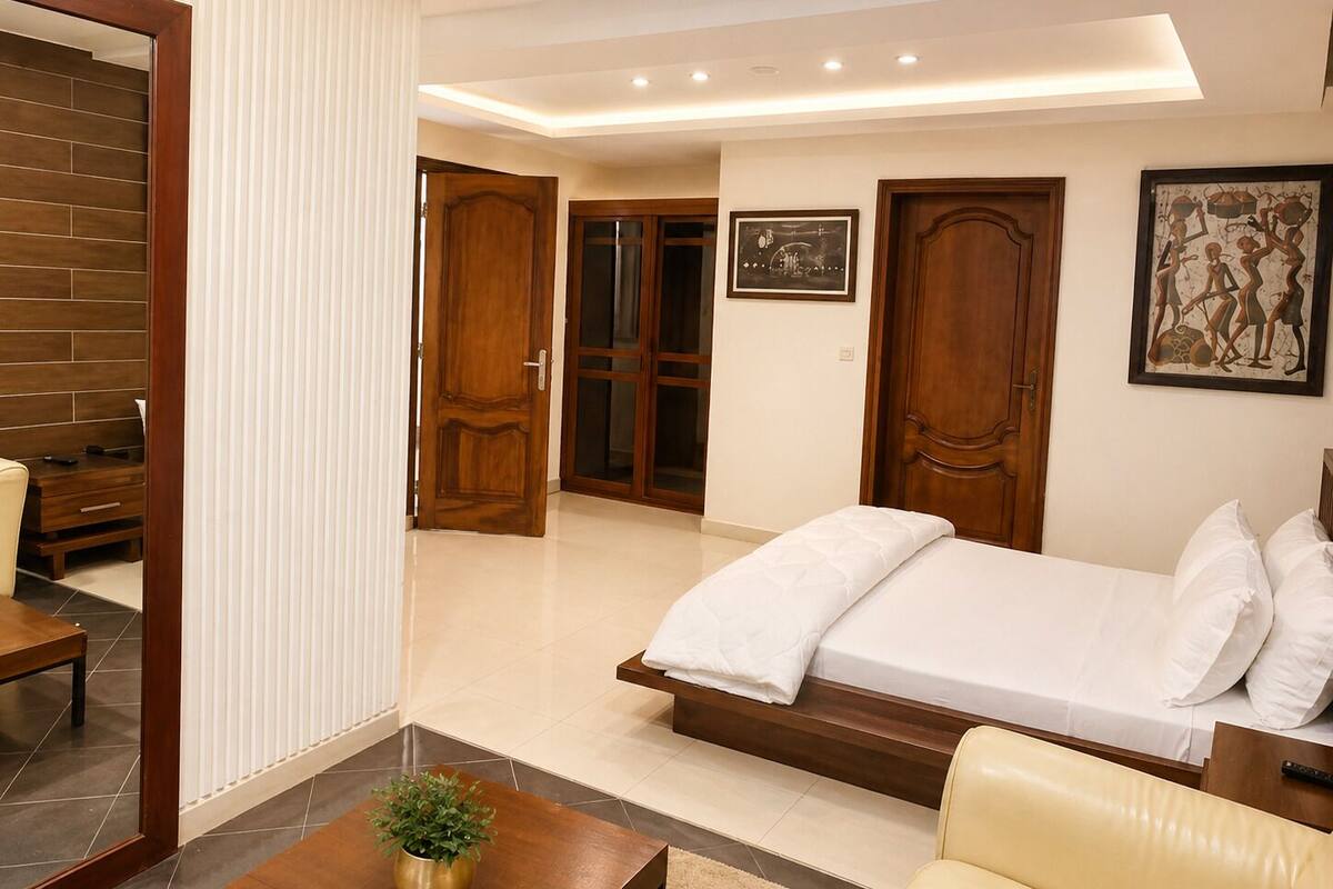 A bedroom with a bed, a sofa, a wooden cabinet, and a door leading to another room.