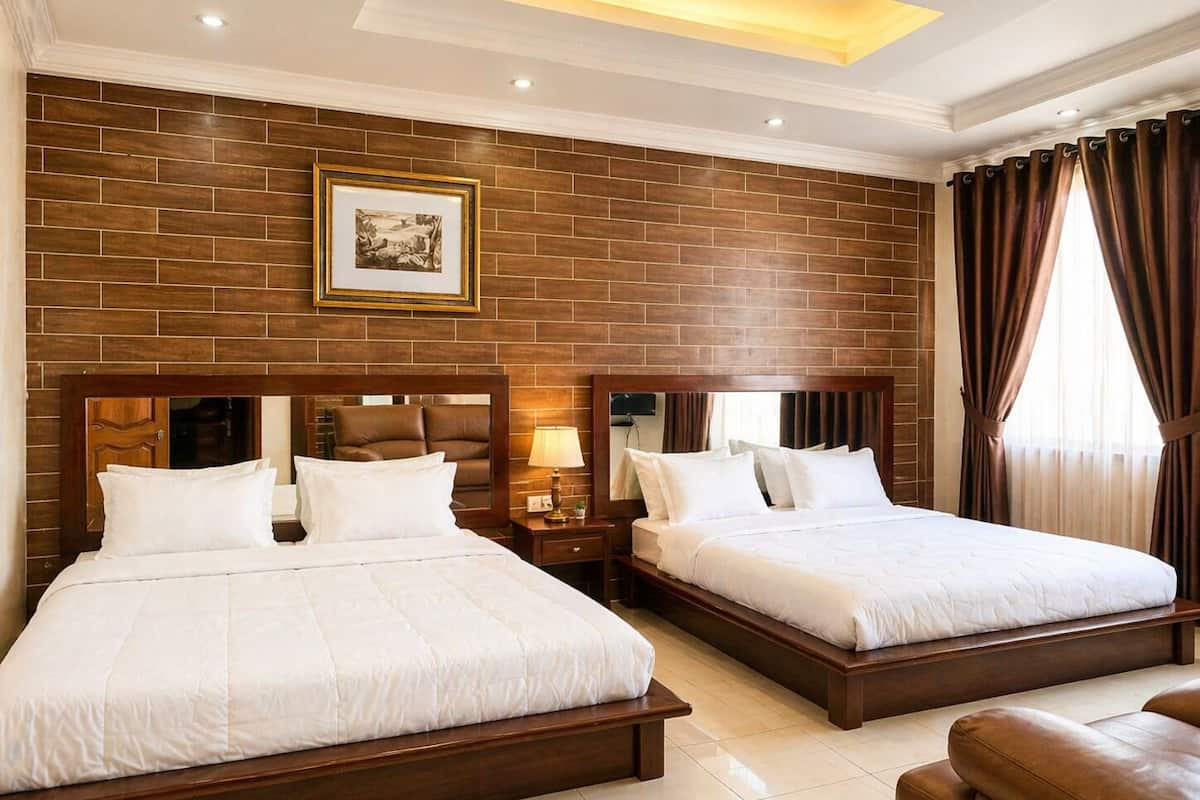 A hotel room with two beds, a wooden headboard, a nightstand with a lamp, a framed picture on the wall, and a window with curtains.