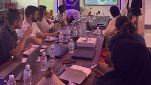 A conference room with a long table, laptops, water bottles, and a presentation screen.