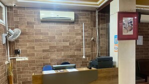 A reception desk with a modern design, a wall-mounted air conditioner, a security camera, and a small plant.