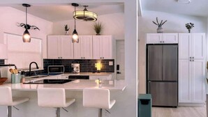 A modern kitchen with white cabinets, a stainless steel refrigerator, and a bar area with white stools. - Private Pool Villa | 5 Min to Disney & Universal (Orlando)
