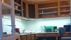 A kitchen with wooden cabinets, a refrigerator, a stove, and a dining area with a chair and table.