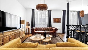 Un salon moderne avec un canapé en cuir, des fauteuils jaunes, une table basse en bois et un téléviseur.