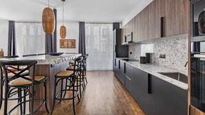 Une cuisine moderne avec des meubles de couleur sombre, un plan de travail en marbre et un îlot central doté de tabourets de bar.