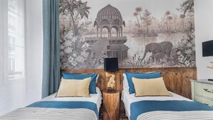 Une chambre avec deux lits, une tête de lit en bois, une table de chevet et une fresque représentant un temple et un éléphant.