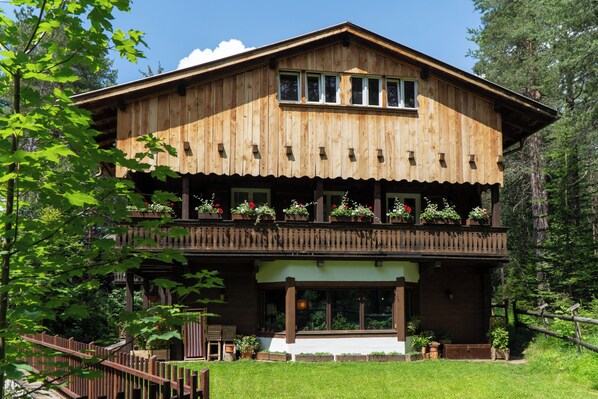 Un chalet de madera con balcón, ventanas amplias y un jardín bien cuidado.
