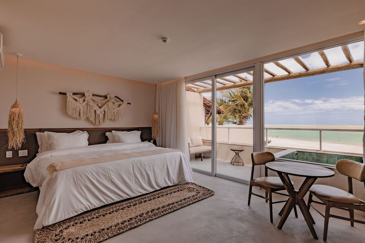 Une chambre avec un grand lit, une vue sur la plage et un balcon équipé d’une table et de chaises.